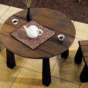 Puede incluir: Una mesa redonda de madera marrón oscuro con una tetera blanca y un pequeño taburete de madera marrón. La mesa tiene una tapa de madera marrón oscuro y patas negras. El taburete tiene una tapa de madera marrón oscuro y patas negras.