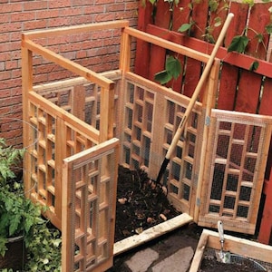 May include: A wooden compost bin with a wire mesh front and a hinged door. The bin is filled with compost and has a shovel leaning against it. There is a small wooden sifter in the foreground.