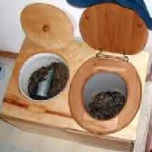 Könnte beinhalten: Eine Komposttoilette aus Holz mit zwei Öffnungen. Eine hat einen runden Deckel und einen Toilettensitz, die andere einen runden Deckel. Beide zeigen dunkles, organisches Material. Die Toilette ist aus hellem Holz gefertigt.