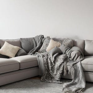 Puede incluir: Un gran sofá seccional gris con múltiples almohadas y una manta de tiro con estampado gris y blanco.