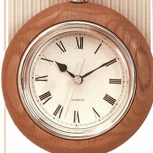 Könnte beinhalten: Eine Holztaschenuhr mit weißem Zifferblatt und römischen Ziffern. Die Uhr hat eine goldfarbene Kette und einen silberfarbenen Rand. Der Text "POCKET WATCH CLOCK" ist unter der Uhr gedruckt.