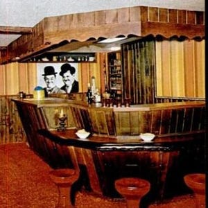 Puede incluir: Una barra de madera con una encimera curva y tres taburetes de bar. La barra está decorada con paneles de madera y un papel tapiz a rayas. Hay una foto de dos hombres con sombreros sobre la barra.