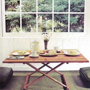 May include: A wooden folding table with a brown tabletop and a criss-cross base. The table is set with plates, cups, and food.