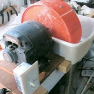 Puede incluir: Un pequeño motor eléctrico negro con una rueda de plástico roja unida a él. El motor está conectado a una toma de corriente blanca. La rueda gira en una tina de plástico blanca.