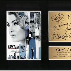 Könnte beinhalten: Gerahmte Grey's Anatomy-Erinnerungsstücke. Die linke Seite zeigt ein Poster mit dem Titel und den Darstellern der Serie. Die rechte Seite enthält eine goldene Tafel mit Unterschriften und ein Namensschild mit den Darstellern. Der Rahmen ist schwarz.