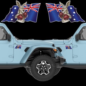 May include: A light blue Jeep with black tyres and rims. The vehicle features two decals of a kangaroo wearing boxing gloves in front of an Australian flag. Smaller Australian flag decals are on the side.
