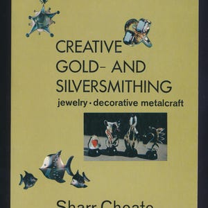 May include: A book cover with a light olive background titled CREATIVE GOLD- AND SILVERSMITHING jewelry • decorative metalcraft by Sharr Choate. The cover features images of a star-shaped pendant, a ring, four small abstract sculptures, and three fish.