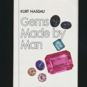 May include: Book cover with the title "Gems Made by Man" by Kurt Nassau. The cover features a variety of colorful gemstones, including a large pink gem, a blue gem, and a green gem.