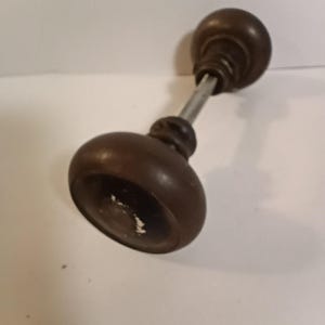May include: A vintage brown wooden door knob with a metal rod. The knob has a rounded shape with a slightly distressed finish. The door knob is likely for a cabinet or a small door.