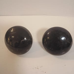 May include: Two dark, glossy, spherical objects with a reflective surface. The spheres are a deep, rich black color and appear to be made of a smooth, polished material. They are set against a neutral background.