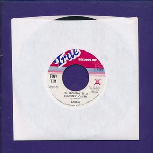 May include: A 7-inch vinyl record in a white paper sleeve. The record label is white with a red and blue top section featuring the text True Records Inc. The center text reads Tiny Tim, I'm Gonna Be A Country Queen, T-109-A, and DJ Copy.