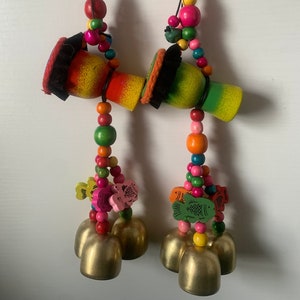 May include: Two colorful wooden wind chimes with bells and beads. Each chime features a small wooden drum with a painted design and a tassel. The beads are in various colors, including red, green, yellow, pink, and blue. The bells are gold and have a shiny finish.