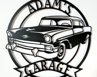 Op de afbeelding: Zwart-wit metalen bord met een klassiek auto-ontwerp. Het bord is cirkelvormig met de woorden "ADAM'S GARAGE" uitgesneden. De auto is een vintage model, ook uitgesneden, met gedetailleerde kenmerken zoals koplampen en een grille.