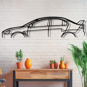 May include: Black metal silhouette of a car mounted on a white brick wall. The car is in profile view and has a sporty design. There are potted plants and a wooden table in the foreground.