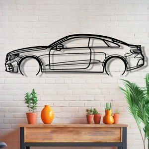 May include: Black metal outline of a car mounted on a white brick wall. The car is a coupe with a sleek design. There are potted plants and a wooden shelf below the car.