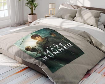 May include: A rectangular blanket featuring the movie poster for "The Maze Runner." The poster shows three young people in a forest setting with the title in white block letters. The blanket is on a bed with neutral-colored bedding.