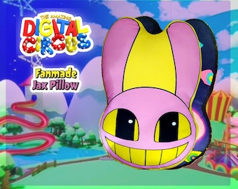 May include: A fanmade Jax pillow from "The Amazing Digital Circus" with a pink face, yellow eyes and teeth, and a yellow and black striped design. The pillow has the text "Fanmade Jax Pillow" on the front.