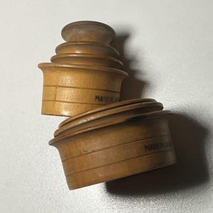 May include: Two wooden stacking toys with a light brown finish. Each toy is composed of several graduated, circular pieces. The text "MADE IN" is visible on the side of one of the toys. The toys are arranged on a white surface.