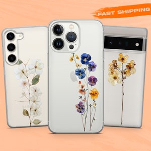 Op de afbeelding: Drie transparante telefoonhoesjes met verschillende bloemenontwerpen. De eerste hoes heeft witte bloemen, de tweede hoes heeft blauwe, paarse en gele bloemen en de derde hoes heeft gele bloemen.