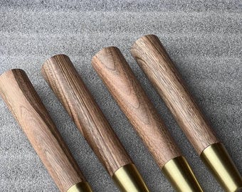 Puede incluir: Cuatro patas de mueble cilíndricas hechas de madera marrón con patrones de veta visibles. Cada pata presenta una tapa de metal cónica y lisa de tono dorado en el extremo inferior, creando un contraste entre la textura de la madera y el metal.