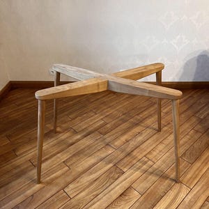 Può includere: Un tavolo in legno chiaro con un piano a forma di X e quattro gambe sottili. Il tavolo ha una finitura naturale venata e un design minimalista. Il tavolo misura circa 61 cm di lunghezza e 30 cm di altezza.