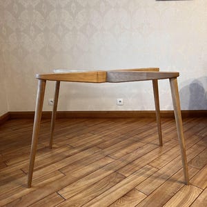 May include: A wooden table with four slender legs. The tabletop is divided into two sections, one light and one medium-toned wood. The table is approximately 40 inches long and 20 inches wide, suitable for a small space or as a side table.