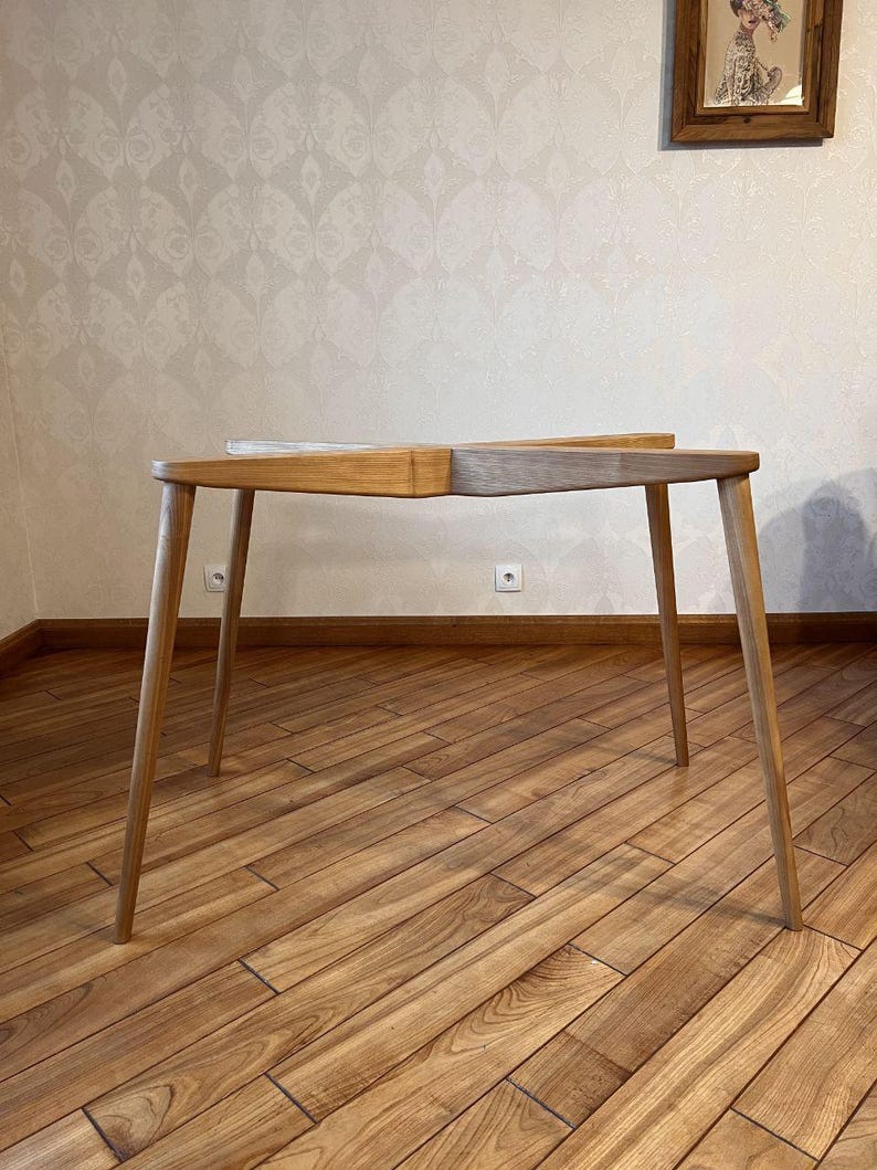 May include: A wooden table with four slender legs. The tabletop is divided into two sections, one light and one medium-toned wood. The table is approximately 40 inches long and 20 inches wide, suitable for a small space or as a side table.