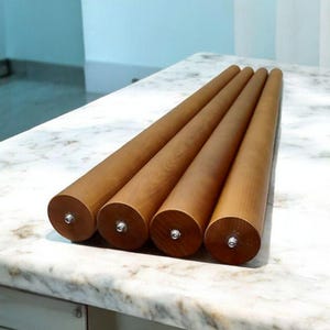 Könnte beinhalten: Vier zylindrische Möbelfüße aus hellem Holz mit silberfarbenen Metallbeschlägen. Die Beine sind diagonal auf einer Marmorarbeitsplatte angeordnet.