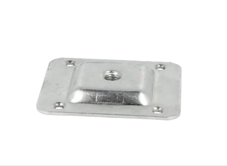 Puede incluir: Una placa cuadrada de metal plateado con un agujero roscado en el centro. La placa tiene cuatro agujeros alrededor del borde.