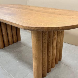 Puede incluir: Una mesa ovalada de madera con una base &uacute;nica hecha de m&uacute;ltiples patas cil&iacute;ndricas. La superficie de la mesa es de un color marr&oacute;n intenso y las patas son de un tono marr&oacute;n ligeramente m&aacute;s claro.