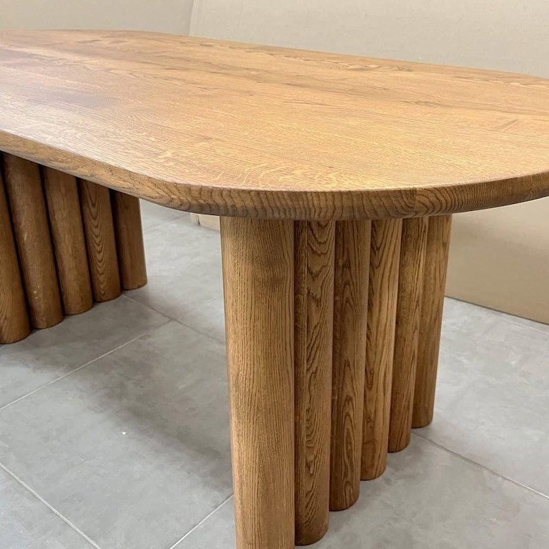 Puede incluir: Una mesa ovalada de madera con una base &uacute;nica hecha de m&uacute;ltiples patas cil&iacute;ndricas. La superficie de la mesa es de un color marr&oacute;n intenso y las patas son de un tono marr&oacute;n ligeramente m&aacute;s claro.