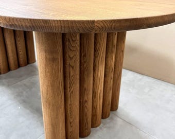 Puede incluir: Una mesa ovalada de madera con una base única hecha de patas de madera cilíndricas apiladas. La superficie de la mesa es de color marrón oscuro y las patas son de un marrón ligeramente más oscuro.