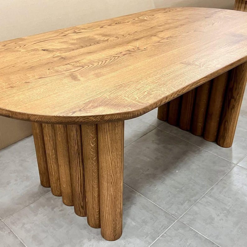 Puede incluir: Una mesa ovalada de madera con una base &uacute;nica hecha de patas cil&iacute;ndricas apiladas. La superficie de la mesa es de color marr&oacute;n oscuro y las patas son de un marr&oacute;n ligeramente m&aacute;s oscuro.