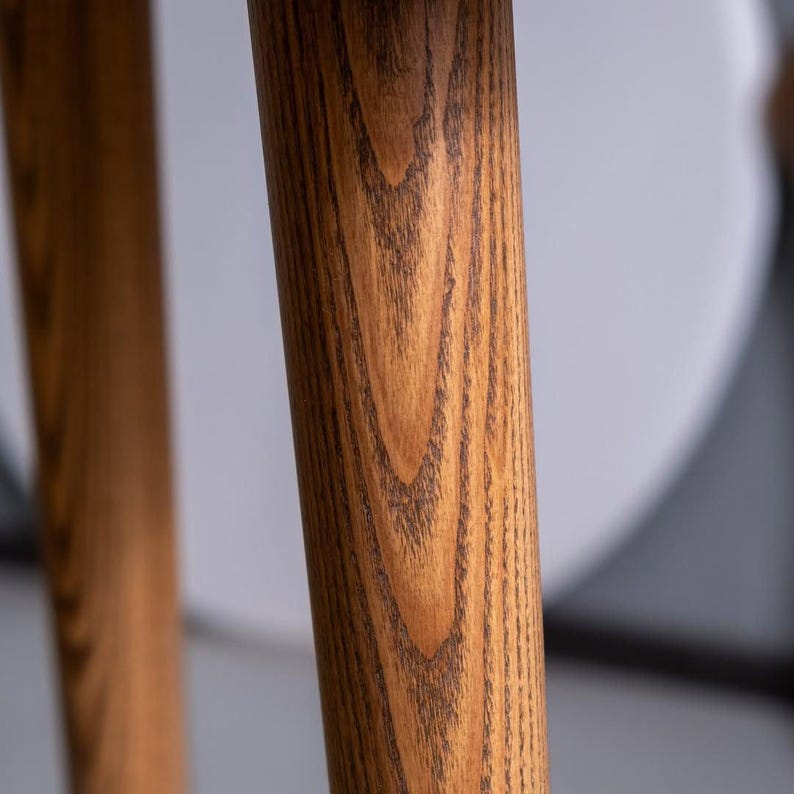 May include: Close-up of two wooden table legs. The legs are a light brown color with a prominent wood grain pattern. The legs are cylindrical and appear to be part of a larger piece of furniture, possibly a table or a chair.