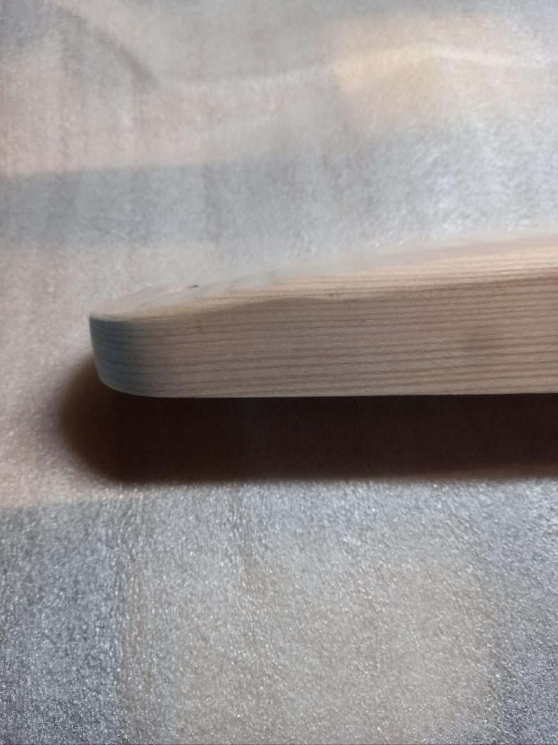 May include: Close-up of a light-colored, unfinished wooden board with rounded edges. The wood grain is visible, and the board appears smooth. The board is likely for crafting or woodworking projects.