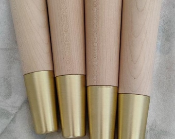 Puede incluir: Cuatro patas de muebles de madera con una punta de metal dorado. Las patas son cónicas y tienen un acabado de madera natural.