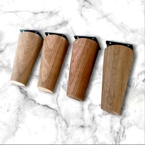 Könnte beinhalten: Vier Holzbeine für Möbel mit schwarzen Metallplatten. Die Beine sind hellbraun und haben eine natürliche Holzmaserung.