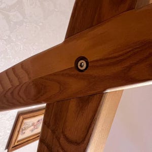 May include: Close-up of a wooden beam joint with a metal fastener. The wood has a warm, brown tone with visible grain. The fastener is a small, circular metal piece set into the wood, providing structural support. The image suggests carpentry or construction.