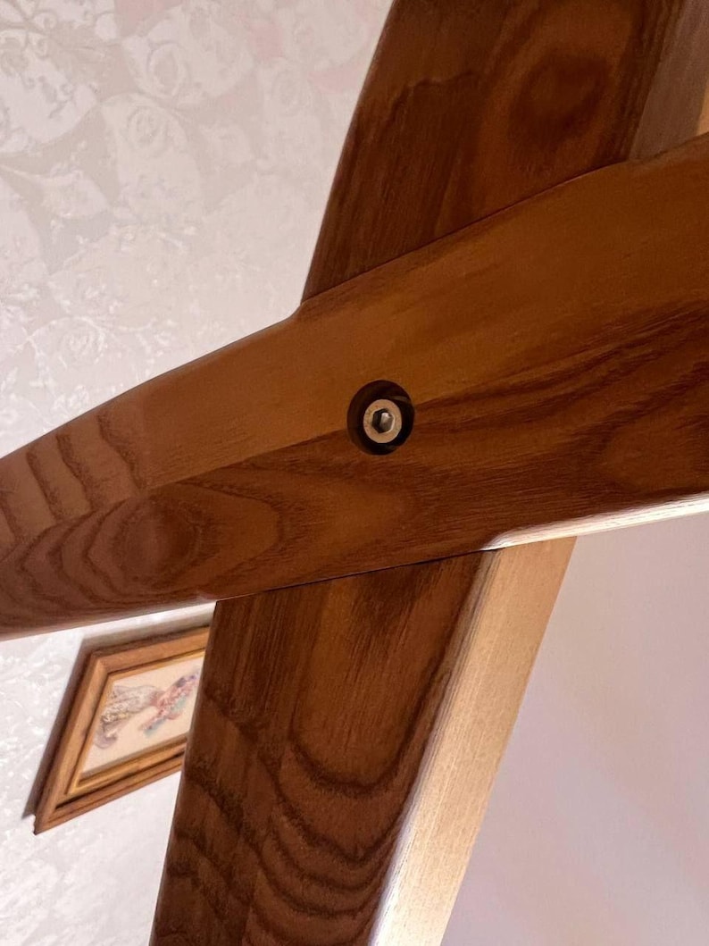 May include: Close-up of a wooden beam joint with a metal fastener. The wood has a warm, brown tone with visible grain. The fastener is a small, circular metal piece set into the wood, providing structural support. The image suggests carpentry or construction.