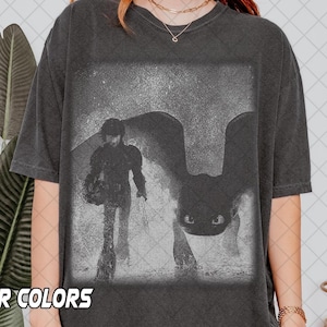 May include: Dark grey t-shirt with a black and white graphic of a person and a dragon. The image is in a faded, vintage style. The shirt has a crew neck and short sleeves. The text "R COLORS" is visible at the bottom.