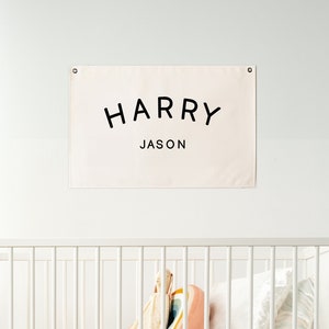 May include: A white crib with a white canvas banner hanging above it. The banner has the text "HARRY JASON" in black lettering.