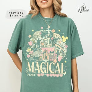 A woman wearing a green t-shirt with a colorful graphic design featuring various Disney-themed elements such as Mickey Mouse, Minnie Mouse, and a castle.