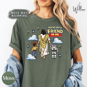 A woman wearing a green t-shirt with a graphic design depicting a cartoon character and a Bible verse.