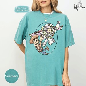 A woman wearing a turquoise t-shirt with a graphic of two characters from the Toy Story franchise, Buzz Lightyear and Woody, on it.