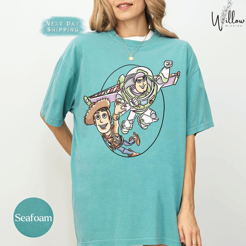 A woman wearing a turquoise t-shirt with a graphic of two characters from the Toy Story franchise, Buzz Lightyear and Woody, on it.