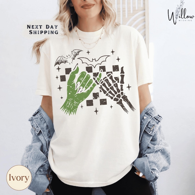 A woman wearing a white t-shirt with a graphic design featuring a bat, skeleton, and checkerboard pattern.