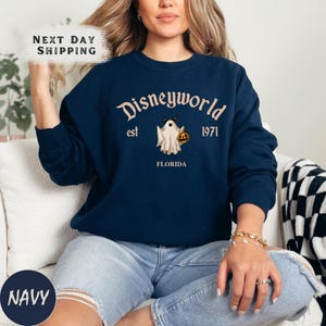 a woman sitting on a couch wearing a disneyland world sweatshirt
