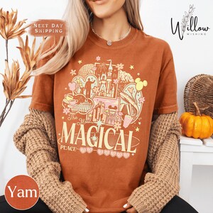 A woman wearing a t-shirt with a colorful graphic design featuring Disney characters and the text "The most magical place".