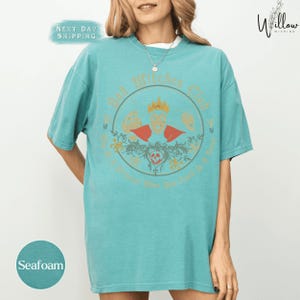 A woman wearing a turquoise t-shirt with a graphic design on it.