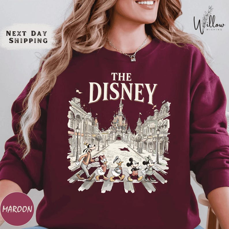 A woman wearing a maroon sweater with a graphic design featuring Disney characters crossing a street.